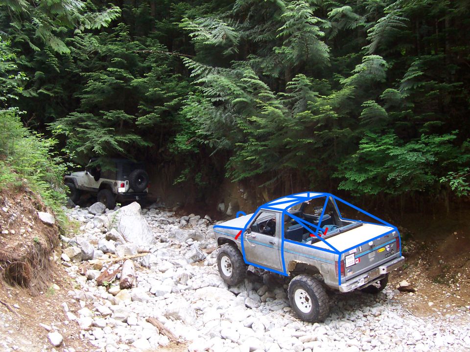 Silver pickup truck with blue roll cage on rocky trail, another Jeep in background