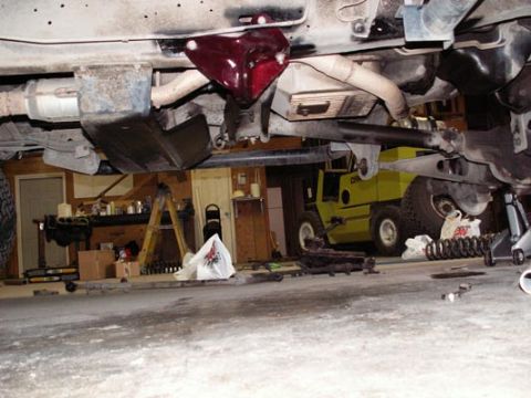 1988 Ford Bronco - Undercarriage view of a vehicle's suspension system, with a forklift in the background.