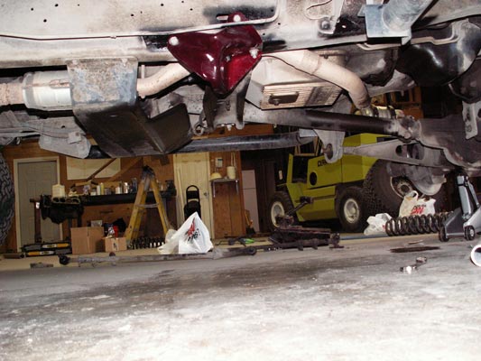 Undercarriage of a vehicle with red suspension bracket and exhaust pipe. Forklift visible in background