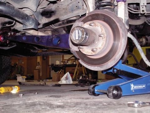 1988 Ford Bronco - Low-angle shot under a truck on a blue Michelin floor jack, showing a purple-powdercoated radius arm with lightening holes, the front axle,…
