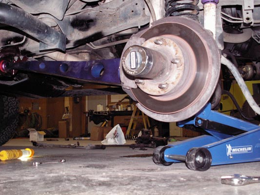 Underside of front axle with purple radius arm, brake rotor and Warn locking hub on a floor jack