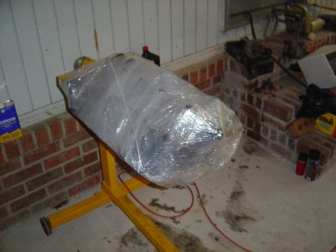 1986 Ford Bronco - Engine block wrapped in plastic and resting on an engine stand, with various automotive supplies in the background.