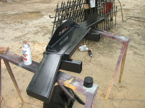 1995 Ford Bronco - A freshly painted black bumper rests on sawhorses outdoors.