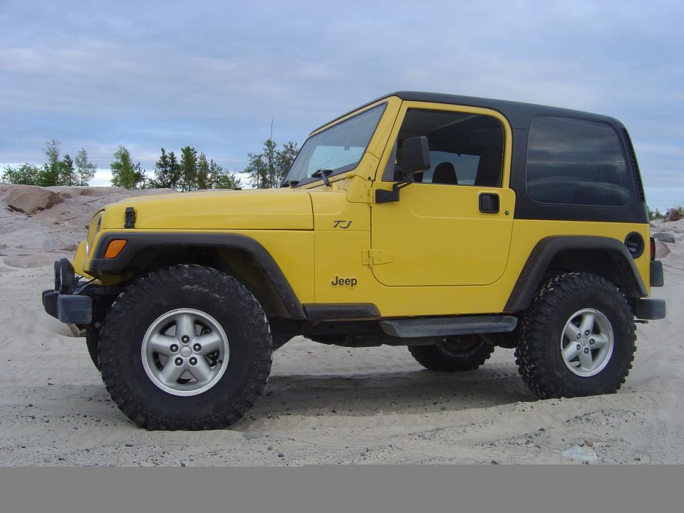Yellow Jeep Wrangler TJ with black hardtop, side view, parked on sand