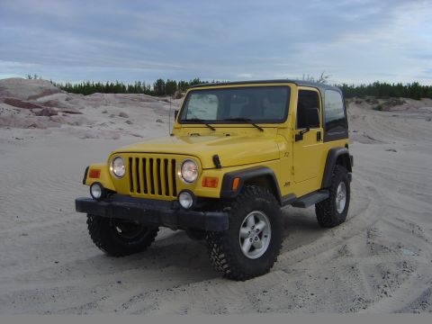 1986 Ford F-150 - A yellow Jeep Wrangler sits on a sandy terrain under a cloudy sky.