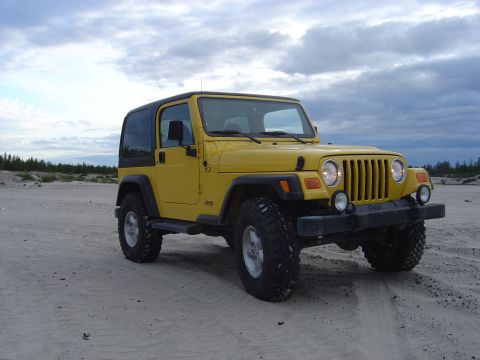 1986 Ford F-150 - Yellow Jeep Wrangler on a sandy beach with a cloudy sky overhead.