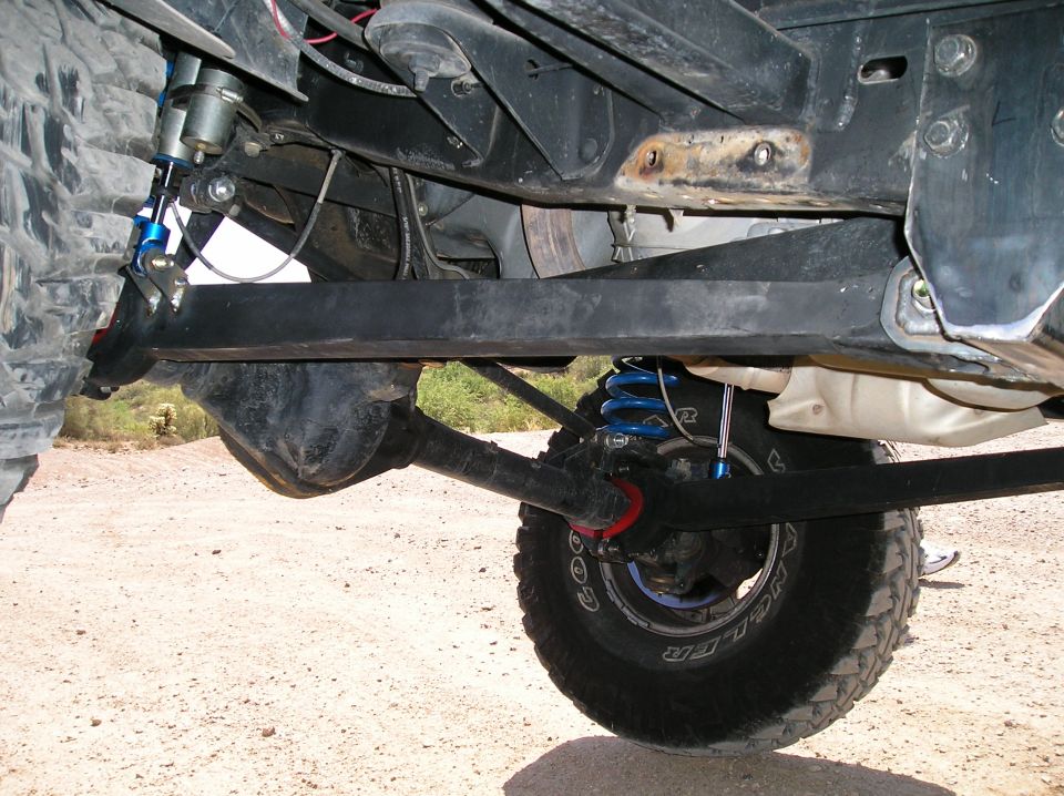 Underside of lifted Bronco showing blue coilovers, black axle, and Goodyear Wrangler tire.