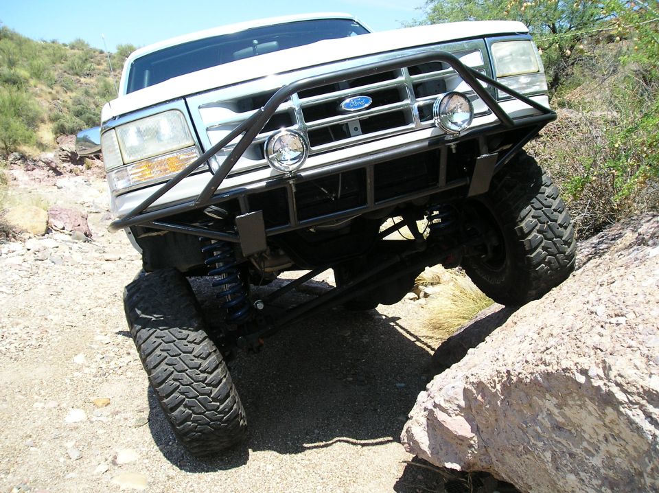 White Ford Bronco with tube brush guard flexing over rocks on desert trail