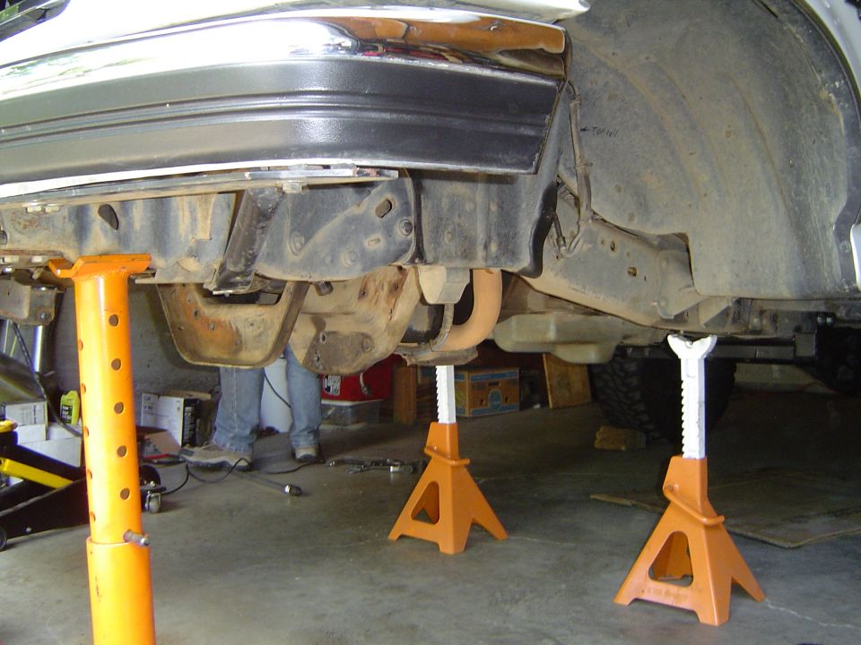 Underside of a vehicle front frame on jack stands showing crossmember and exhaust in a garage