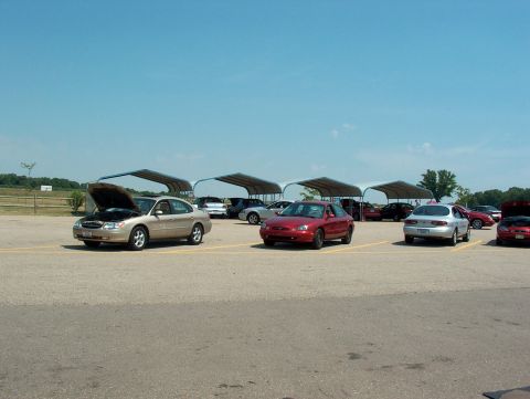 1998 Ford Taurus - Several cars are parked in a lot under canopies, with one 1998 Ford Taurus having its hood open.
