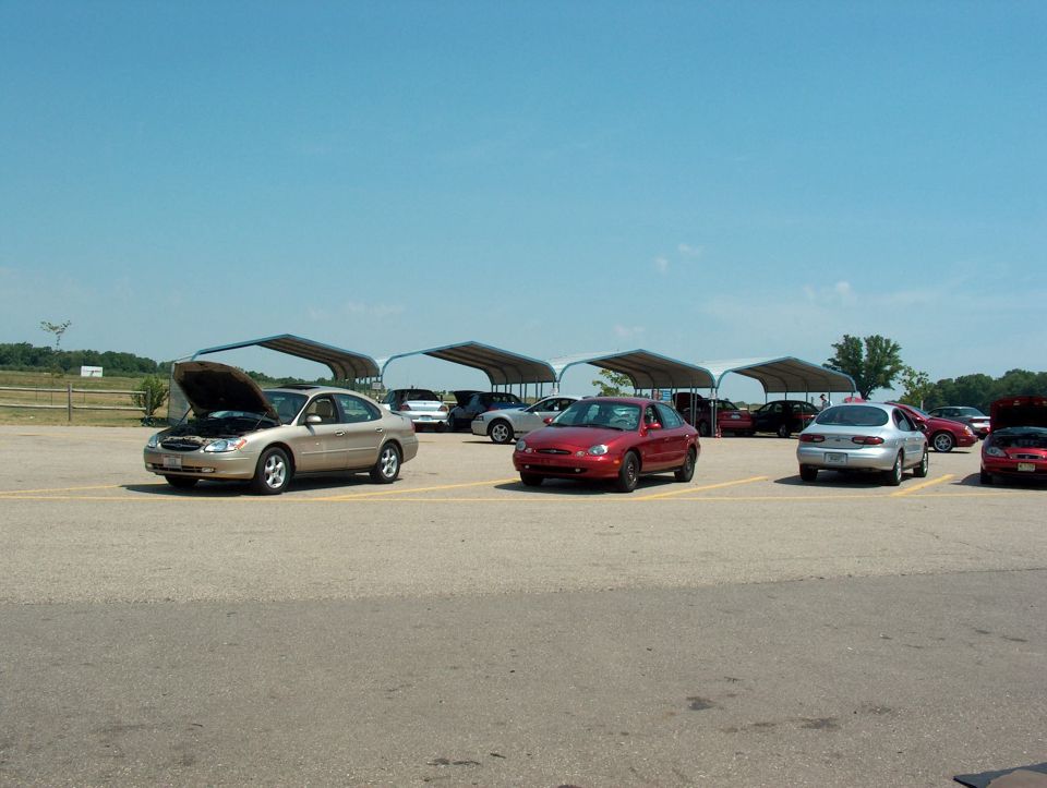 1998 Ford Taurus with hood open parked in lot with other cars under canopies