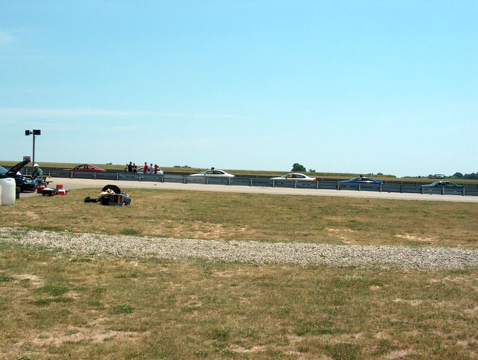 Several cars are lined up on a racetrack with a clear blue sky overhead