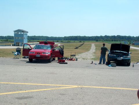 1998 Ford Taurus - Two cars are parked with their hoods and doors open, possibly undergoing maintenance at a racetrack.