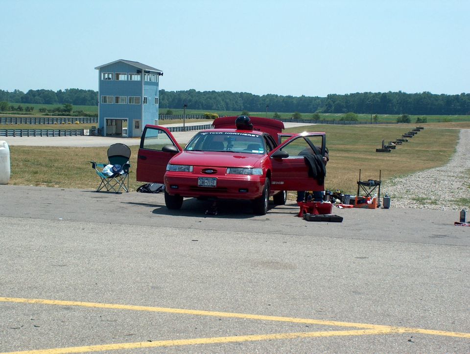 Red 1998 Ford Taurus with doors and hood open, parked at a racetrack