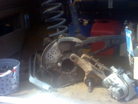 1989 Ford Bronco - Close-up view of disassembled vehicle suspension parts, including a coil spring, shock absorber, and brake components.
