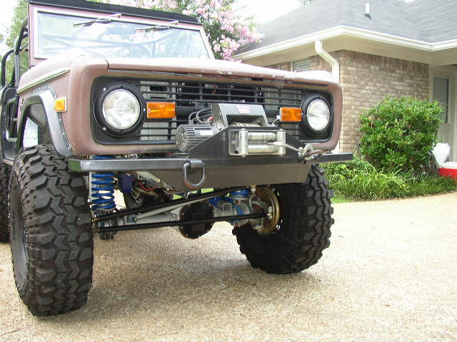 1978 Ford Bronco front end with custom bumper and winch. Large off-road tires and blue suspension components are visible