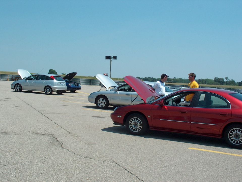 Red sedan with hood open, side view. Other cars visible