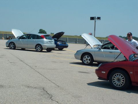 1998 Ford Taurus - Multiple vehicles with hoods open on a paved surface under a clear sky.
