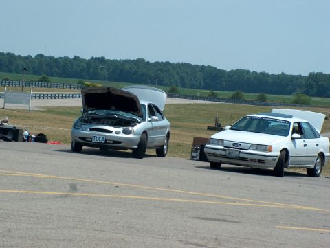 1998 Ford Taurus - Two Ford Taurus sedans are parked on a track with their hoods open, suggesting mechanical attention.
