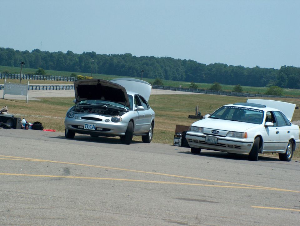 Silver and white Ford Taurus sedans parked on a track, hoods up