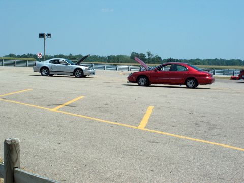 1998 Ford Taurus - Two cars, a silver Ford Mustang and a red sedan, are parked on a racetrack with their hoods open.