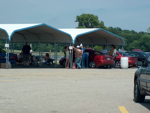 1998 Ford Taurus - People gather under a canopy next to several cars at an outdoor event.