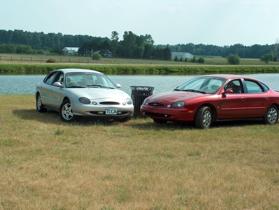 Silver 1998 Ford Taurus and red sedan parked by a lake
