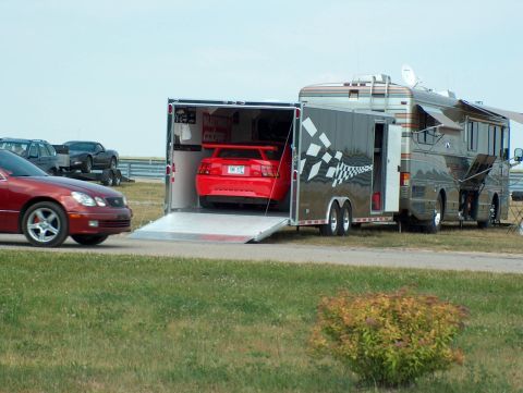 1998 Ford Taurus - A red sports car is being loaded into a trailer, with an RV parked nearby and another car passing.