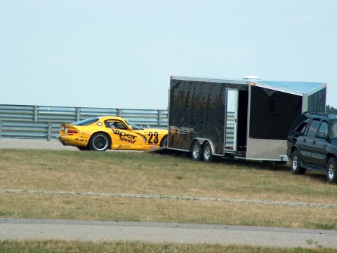 1998 Ford Taurus - A yellow race car numbered 23 is parked next to a black trailer, with a dark SUV visible on the right side.