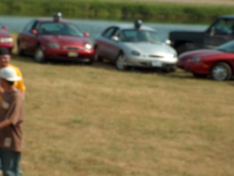 1998 Ford Taurus - A red 1998 Ford Taurus sedan is parked on a grassy field alongside other vehicles.
