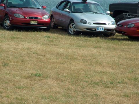 1998 Ford Taurus - Three cars are parked on a grassy area near the water. The silver sedan in the middle appears to be a 1998 Ford Taurus.