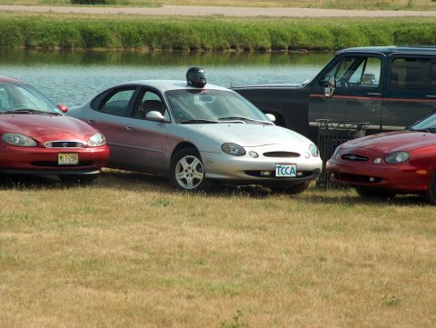 1998 Ford Taurus - Three 1998 Ford Taurus sedans and a dark SUV are parked on a grassy area next to a lake.