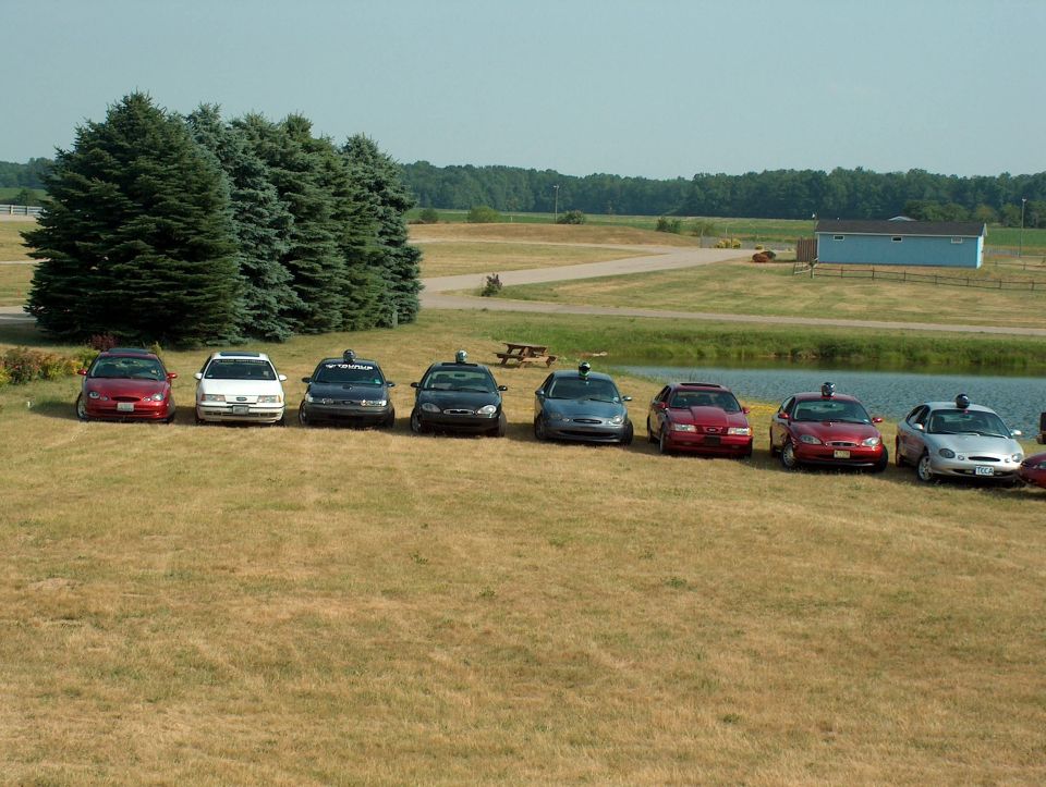 Eight sedans parked in a row on a grassy field