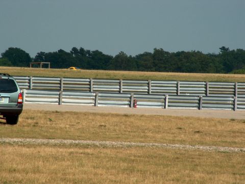 1998 Ford Taurus - A light green SUV is parked on the grass next to a racetrack, with a yellow car visible in the distance.
