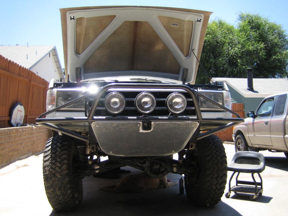 Front of a lifted truck with open hood and a tubular bumper holding three driving lights