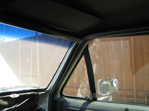 1990 Ford Bronco - From inside a truck cab, the windshield pillar, sun visor and side mirror frame a view of a wooden fence outside.