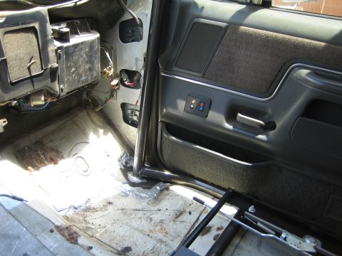 1990 Ford Bronco - partially stripped vehicle interior shows the bare floor, an exposed HVAC box, a grey door panel and a black roll bar tube.