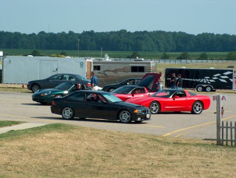 1998 Ford Taurus - A collection of vehicles are parked together, with trailers and trees visible in the background under a clear sky.