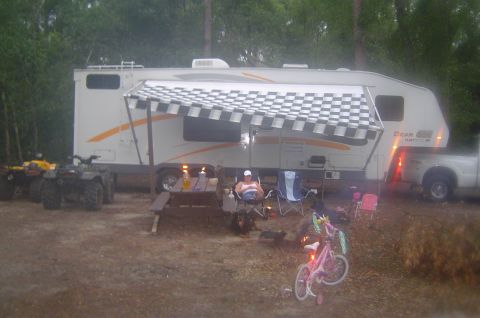 2003 Ford F-350 - A 2003 Ford F-350 pickup truck is seen towing a fifth wheel camper at a campsite, with ATVs and bicycles present.