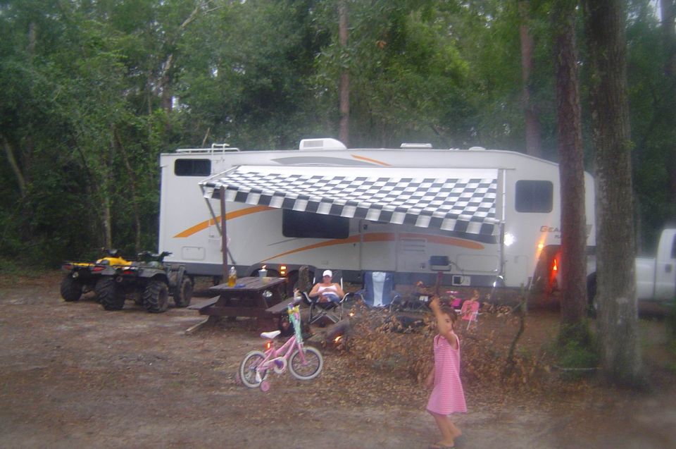 Campsite scene with an RV, two ATVs, a picnic table, and children playing