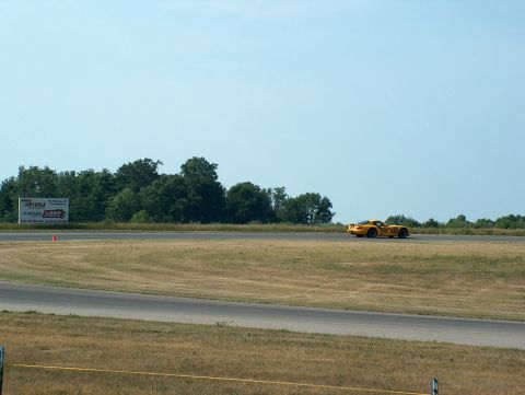 1998 Ford Taurus - A yellow sports car drives on a racetrack with trees and a billboard in the background.