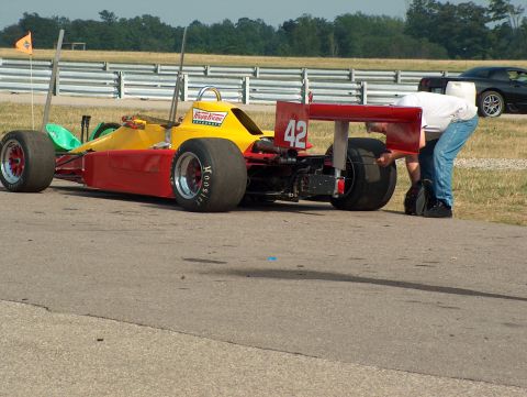 1998 Ford Taurus - A person adjusts the tire on a red and yellow open-wheel race car, with another car visible in the background.