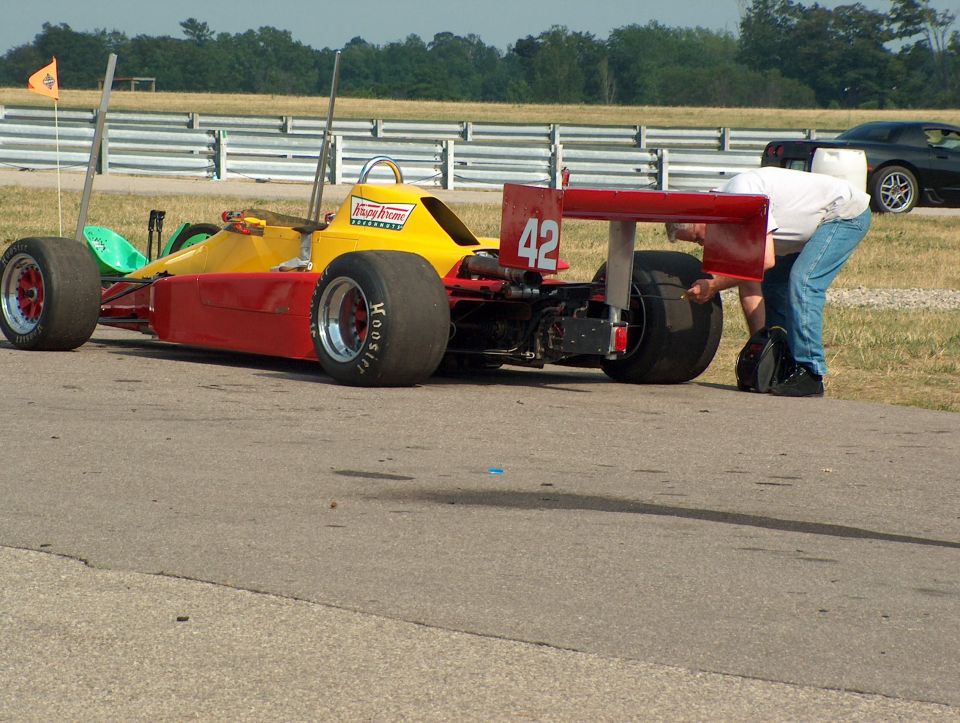 Red and yellow open-wheel race car with number 42 on the rear wing, a person works on the tire