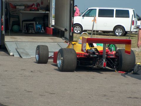 1998 Ford Taurus - A race car is parked on asphalt, with a trailer and a white van in the background.