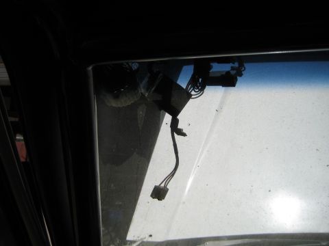 1990 Ford Bronco - close-up of an upper window frame corner showing exposed black wiring and a white electrical connector dangling against the glass.