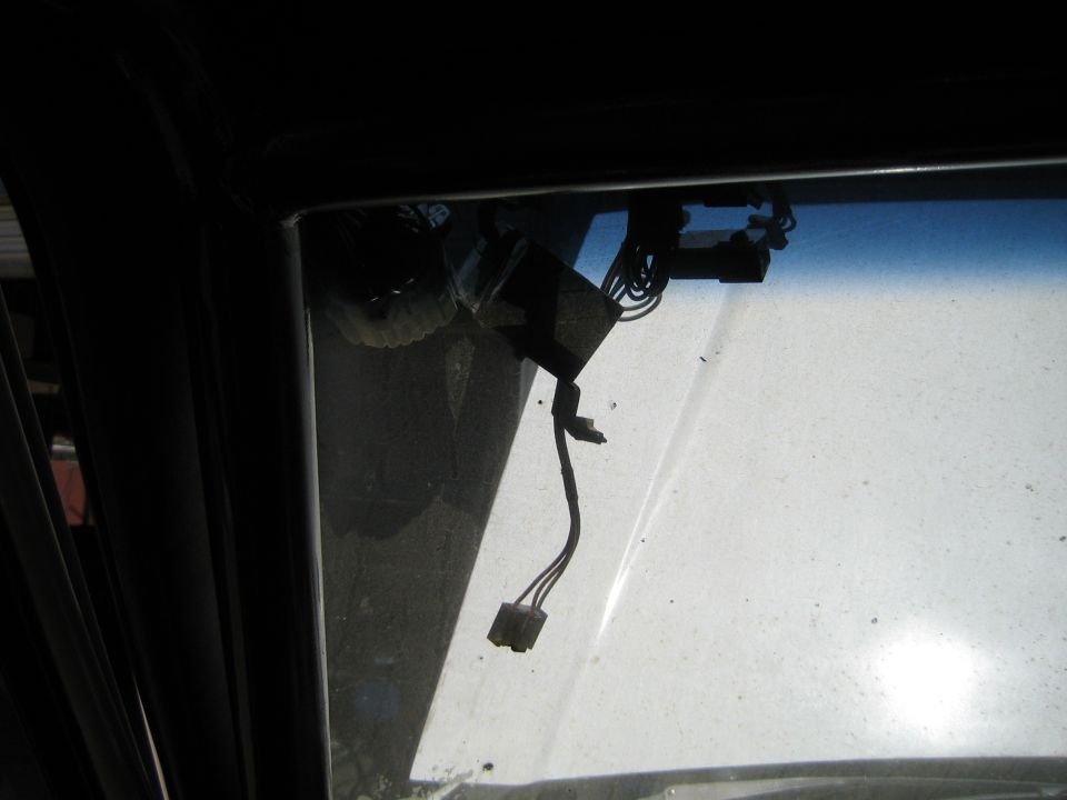 Close-up of a vehicle window frame corner with wiring and connector hanging down