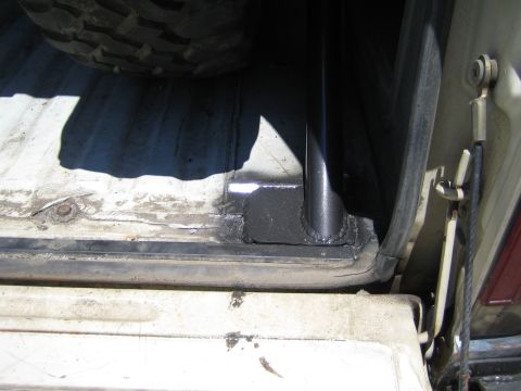 1990 Ford Bronco - black welded tube is bolted to a reinforced plate on the corrugated bed floor of a vehicle near the open tailgate.