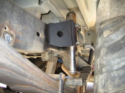 1990 Ford Bronco - underbody view of a vehicle showing a fabricated black shock mount bracket, a polished shock shaft, leaf spring, and frame rail.