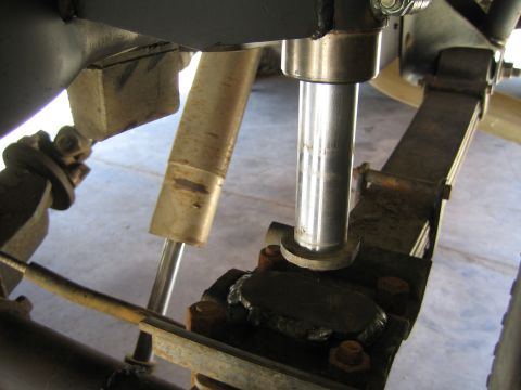 1990 Ford Bronco - close-up under a vehicle showing a polished shock absorber shaft mounted to a bracket beside a limit strap and leaf spring.