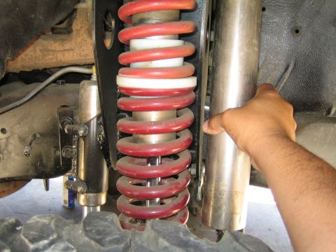 1990 Ford Bronco - hand points to a red coilover spring next to a polished reservoir shock body mounted in a vehicle's suspension.